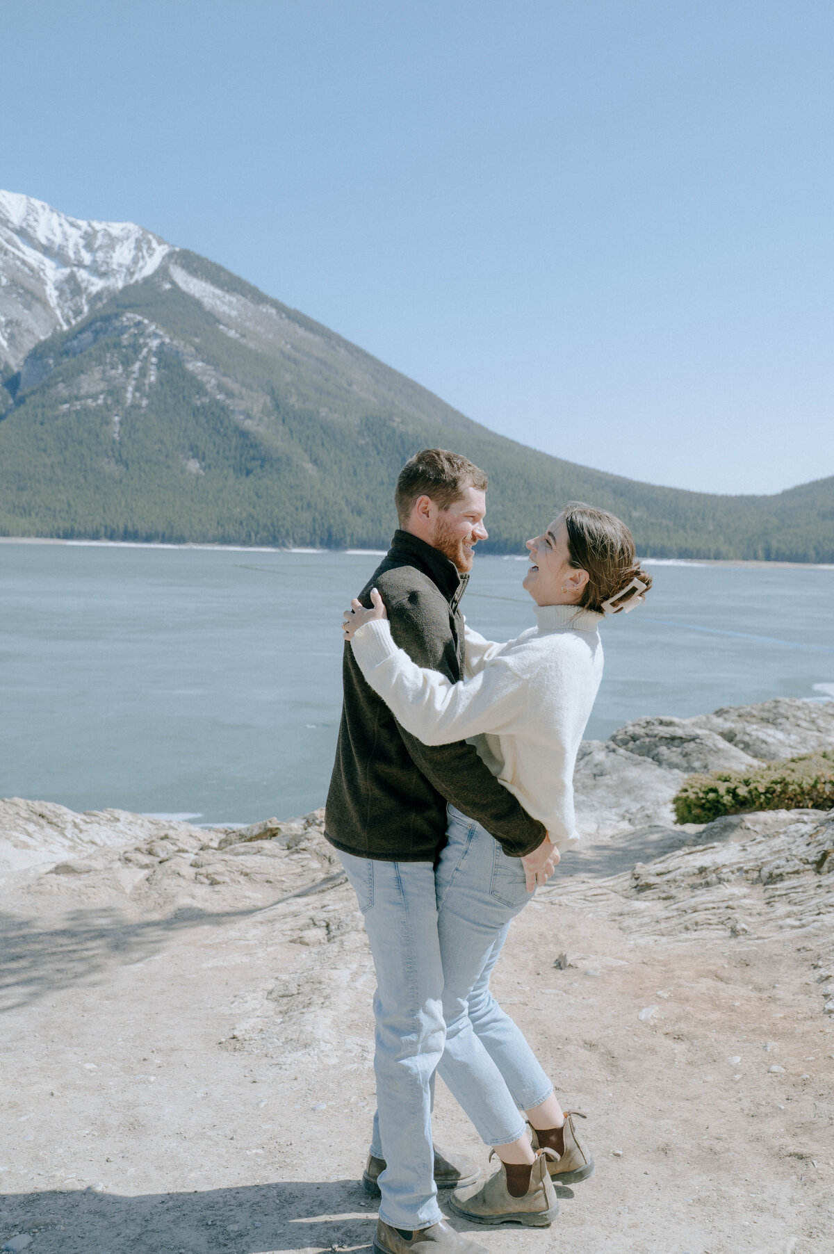 Candid moment as couple dances by Lake Minnewanka with towering peaks behind.