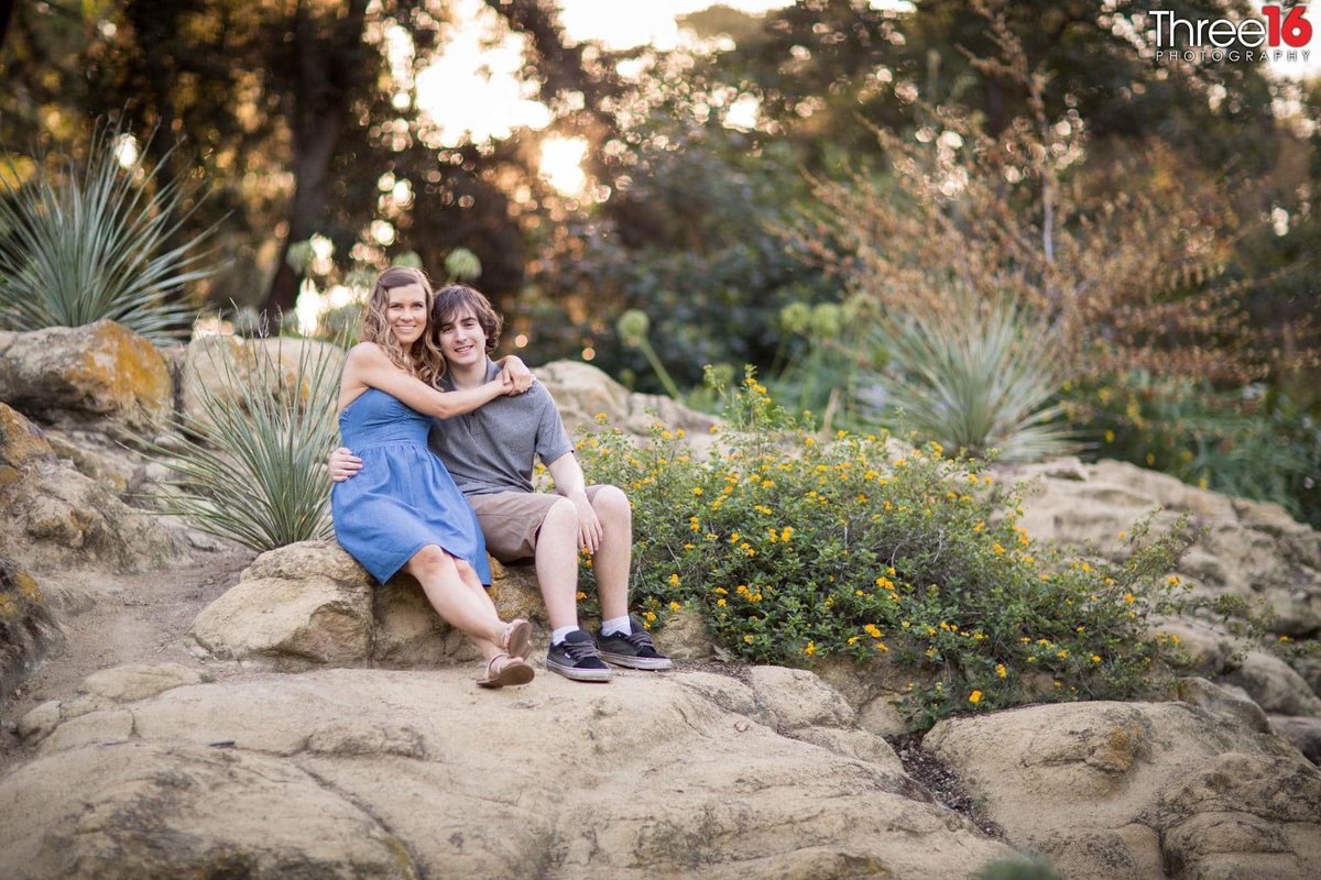 Engaged couple sit together on a large stone at UC Irvine