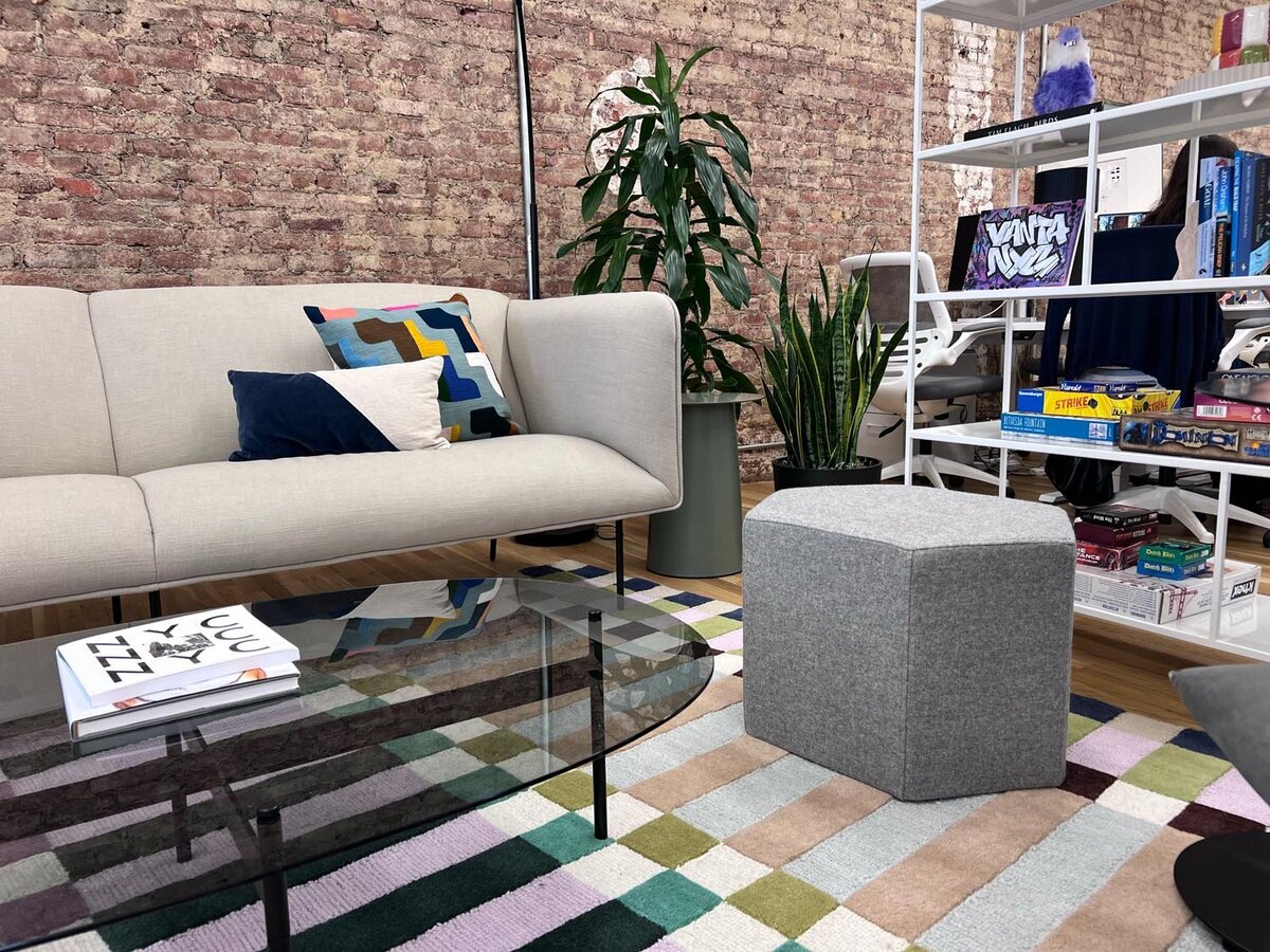 Lounge area with neutral sofa, colorful pillows, geometric rug, glass coffee table, and exposed brick wall.