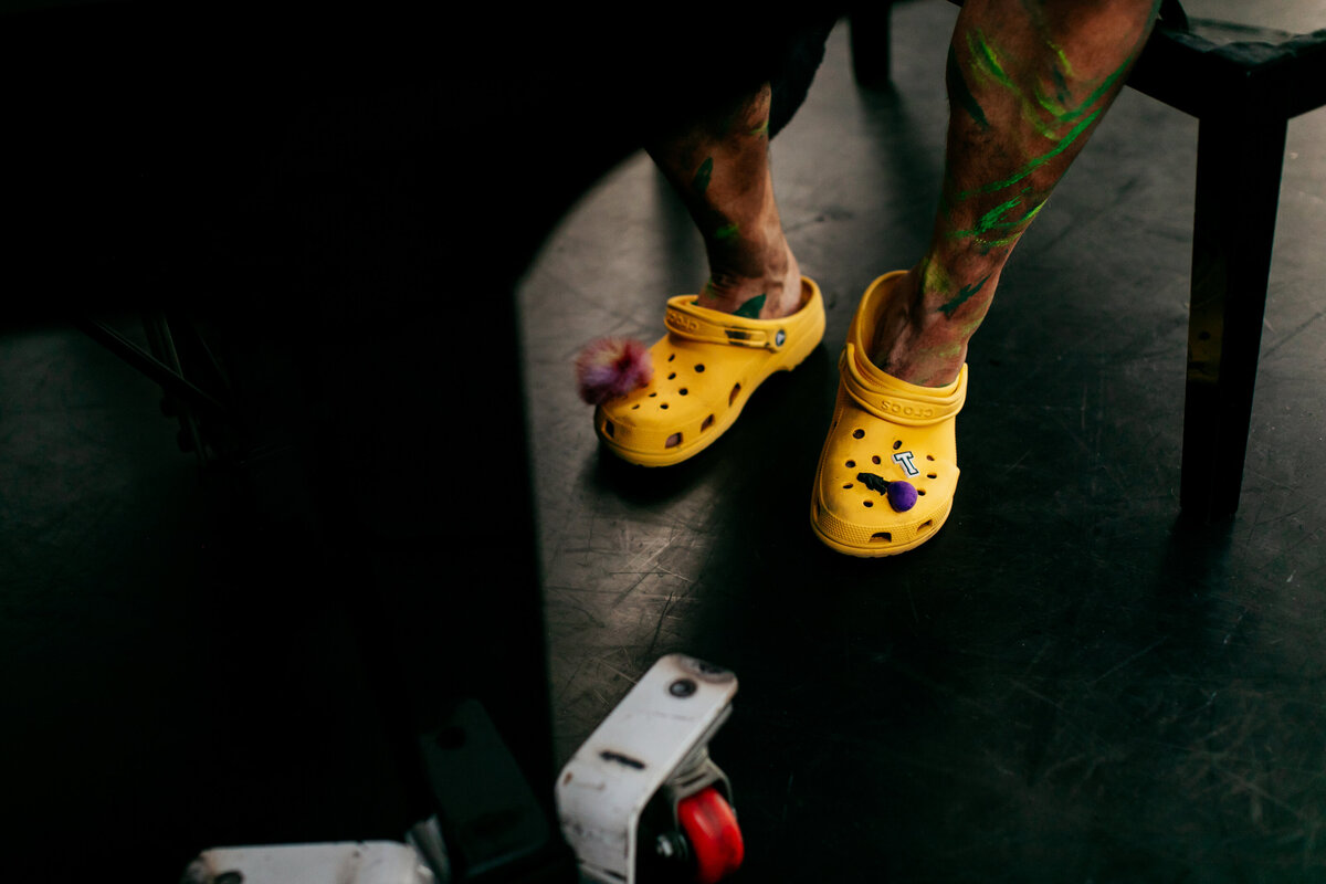 Backstage foto van acteur achter piano met gele crocs aan.