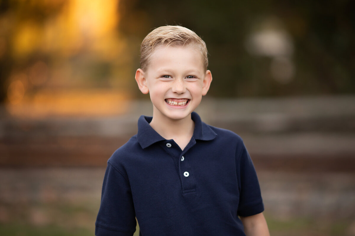 A young boy smiles brightly during a family photoshoot with a Dallas childrens photographer, capturing his joy in the outdoors.