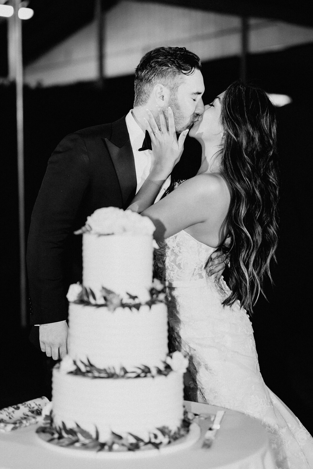 Bride and groom kissing behind their cake in black and white