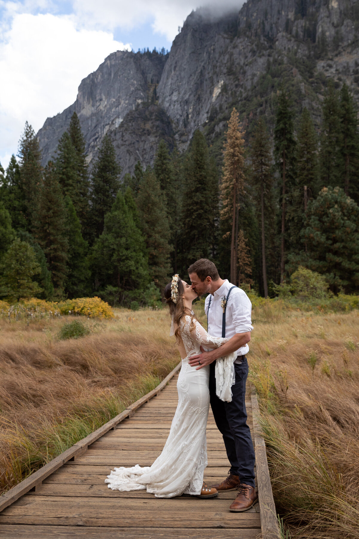 A bride and groom kiss while standing on a wooden boardwalk in a meadow in Yosemite.