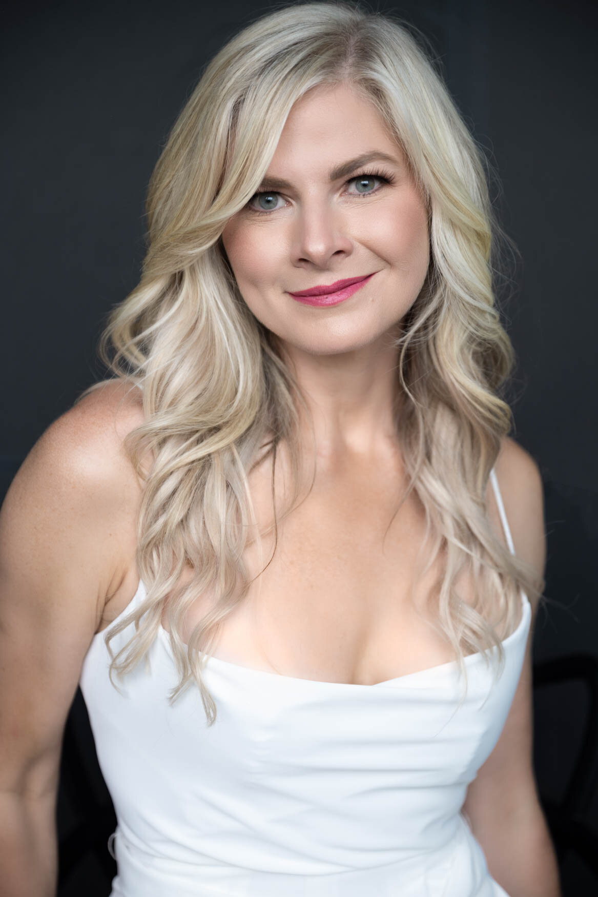 a headshot of a blonde woman smiling to the camera wearing a white tank top