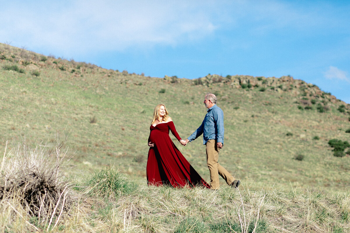 couple walk on a green hillside during their golden colorado maternity photos