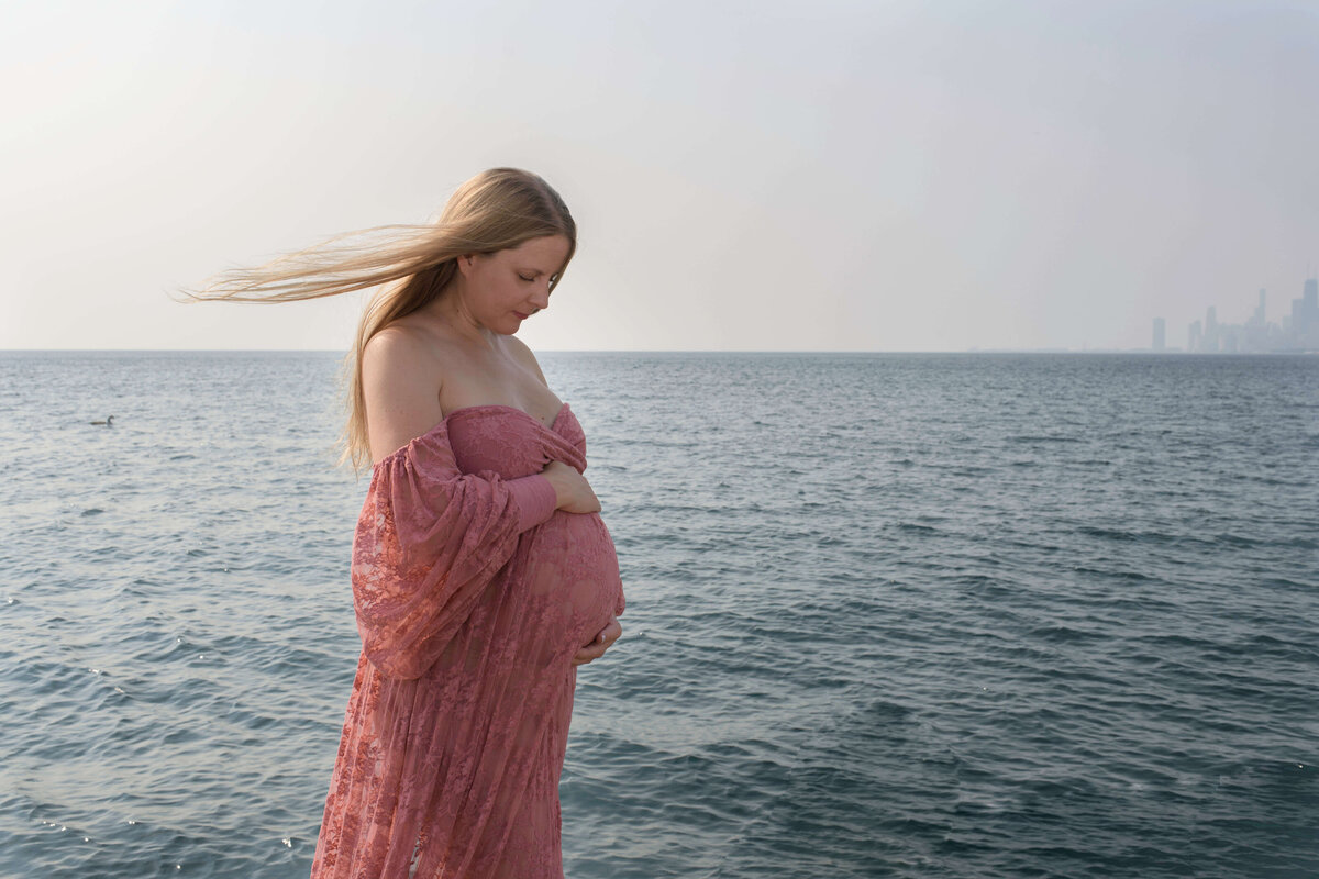 Pregnant woman wearing a pink dress by the lake