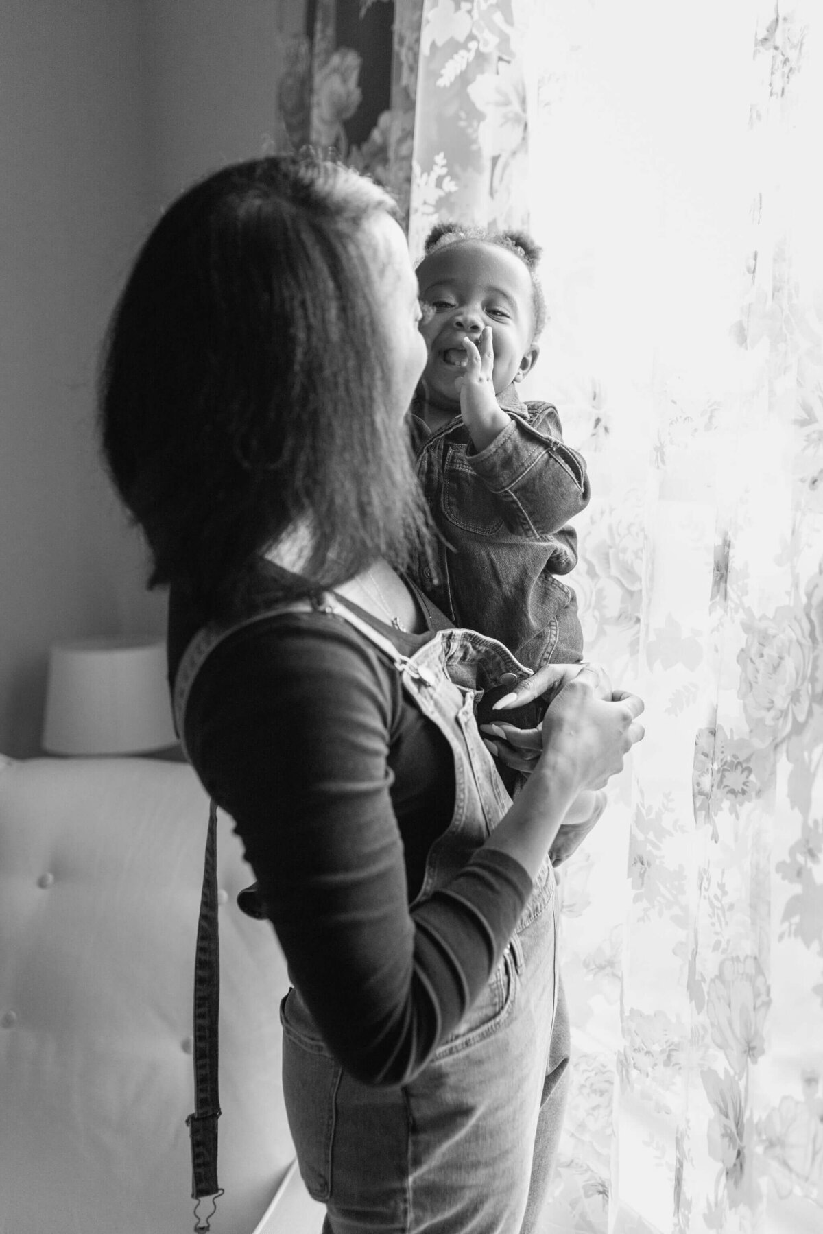 black and white photo of mother and daughter in newborn nursery window during in home lifestyle photography session