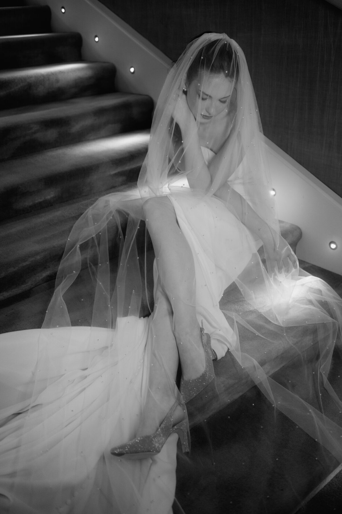 Von dem langen Schleier umhüllt, sitzt das Brautmodel nach unten blickend auf Treppenstufen.
