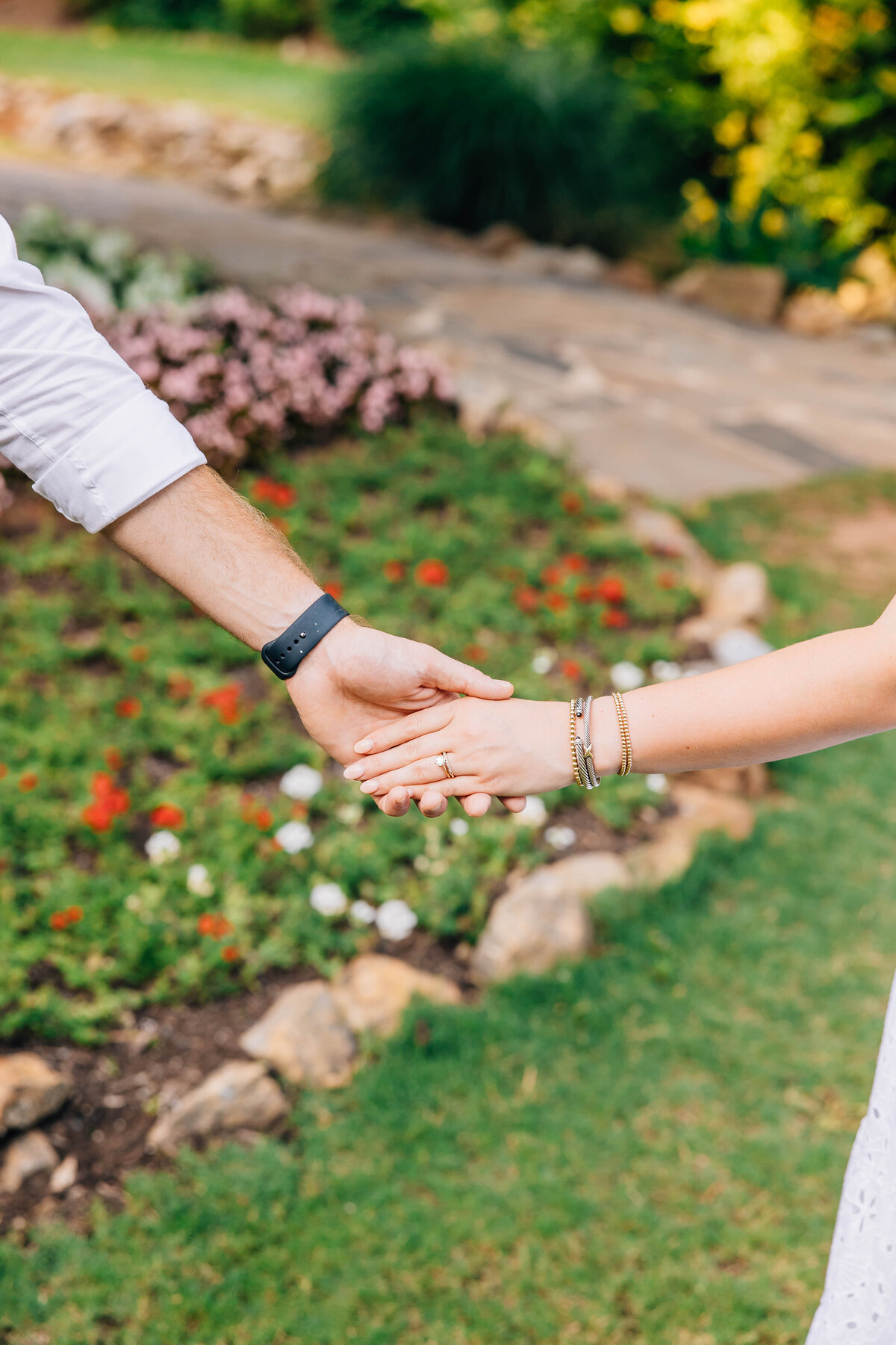 hand shot of engagement ring with couple holding hands