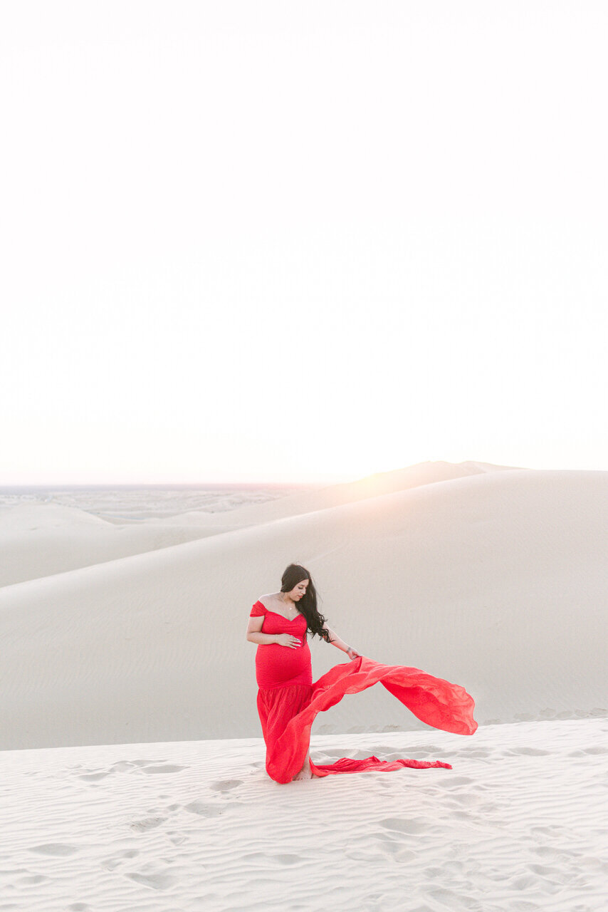 A mother-to-be in a flowing red gown at the Glamis Sand Dunes, captured in a refined editorial style by Elizabeth Kane Photography—serving Philadelphia, New York, and DC.