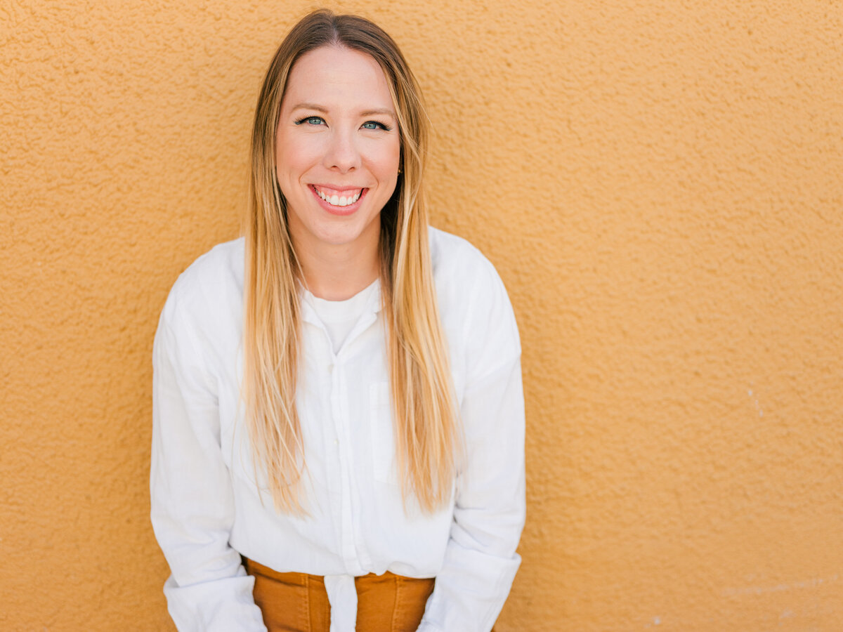 Woman business owner smiling in front of a yellow wall