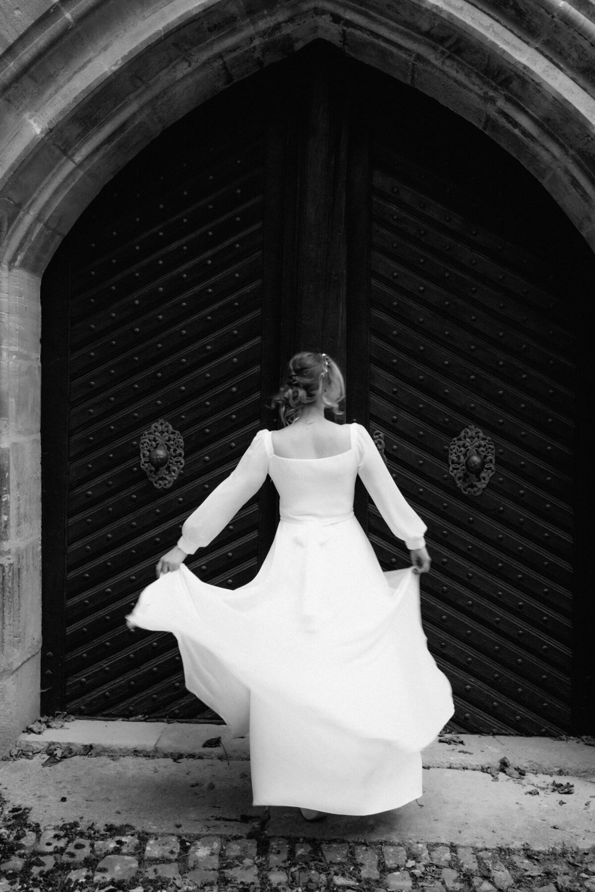 Mit beiden Händen hält die Braut ihr Kleid während sie sich vor dem Tor dreht.