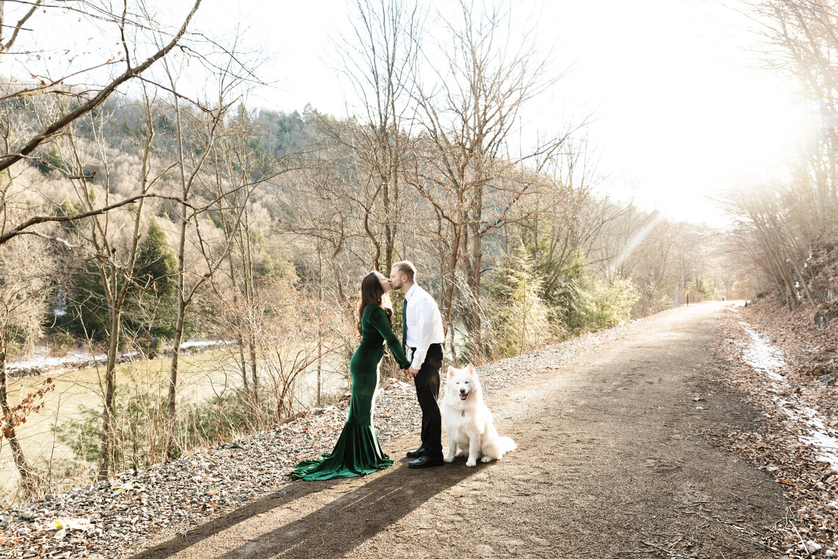 bride and groom kiss on pathway at sunset with their dog sitting at their feet