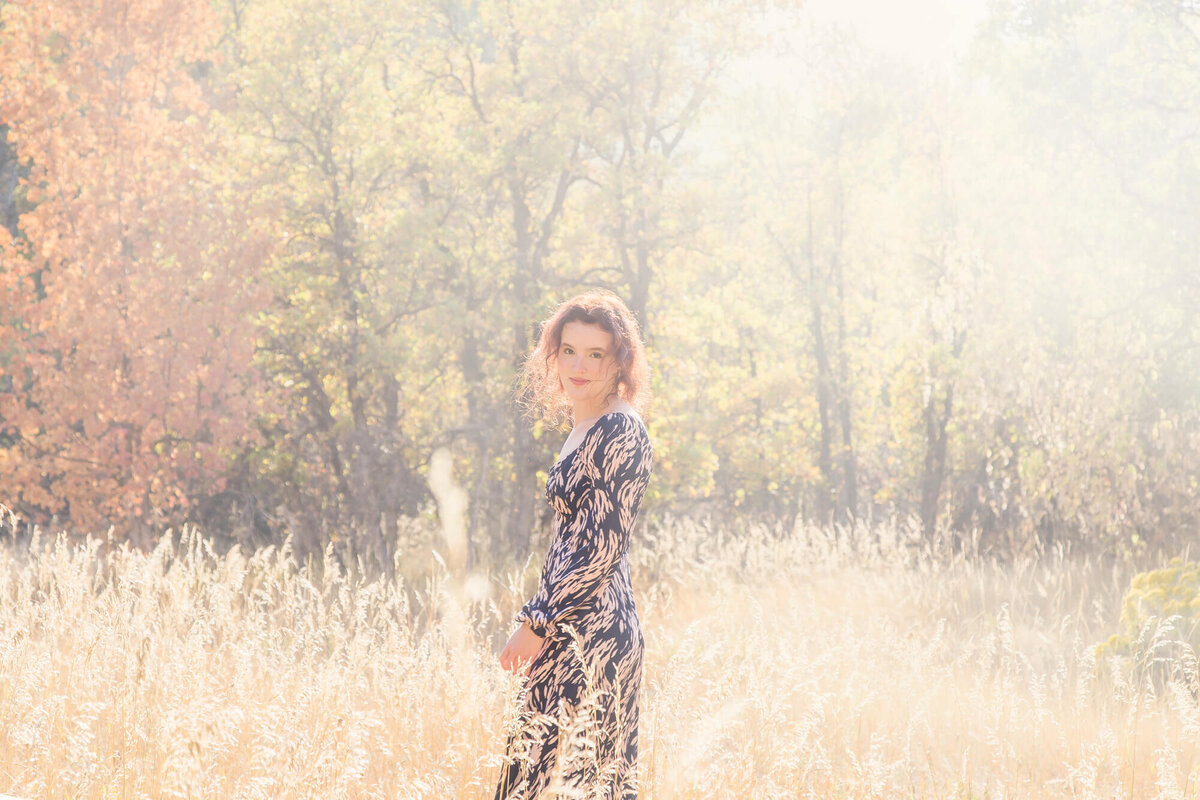 Hazy backlighting behind a redheaded young woman standing in a woodland field