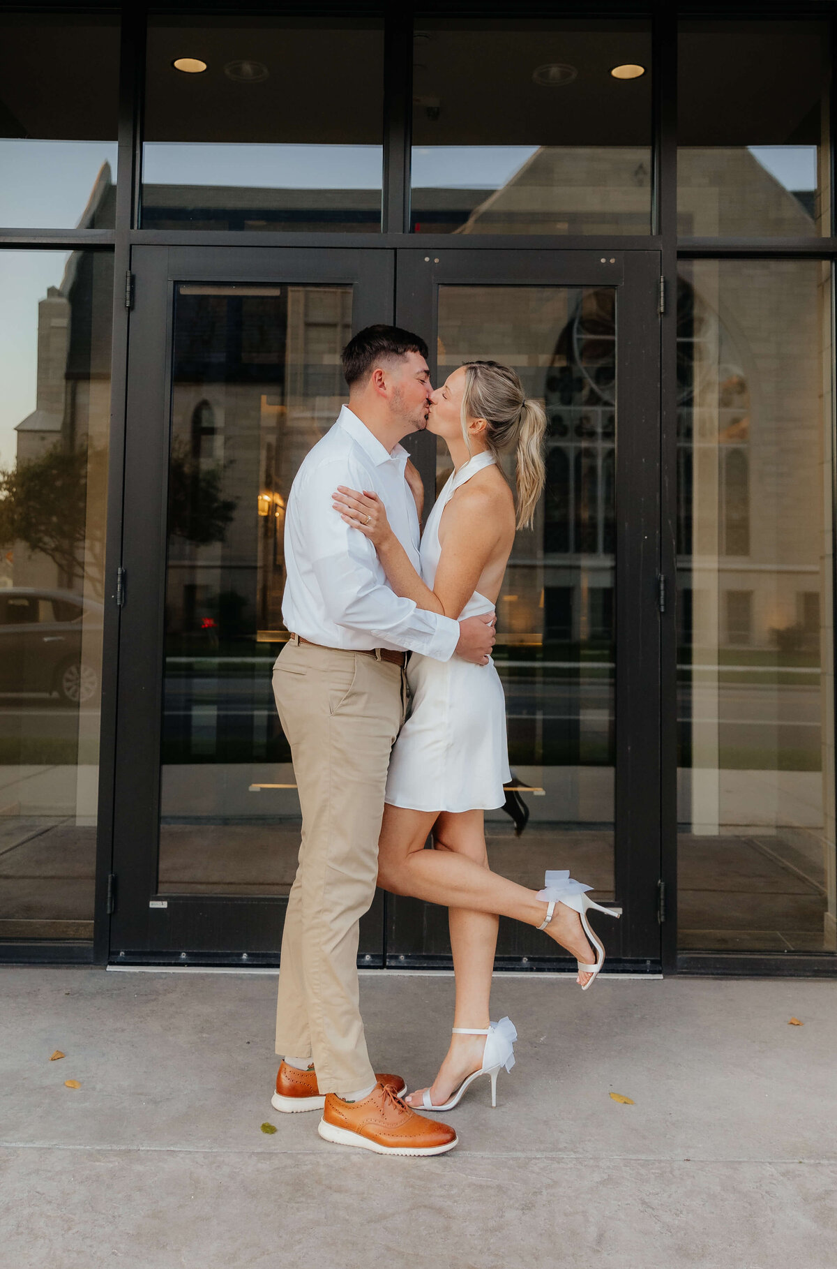 Modern couple kissing in front of glass doors, stylish downtown Michigan engagement photos for playful, sentimental Midwest couples