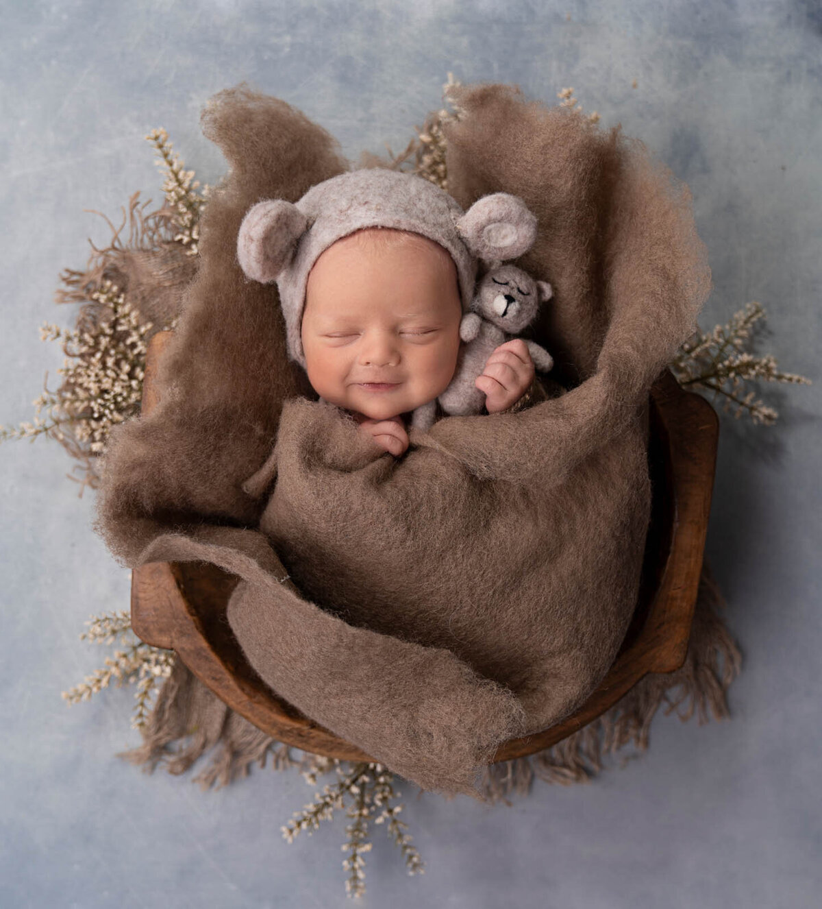 Newborn in brown blanket with stuffed animal bear smiling and sleeping