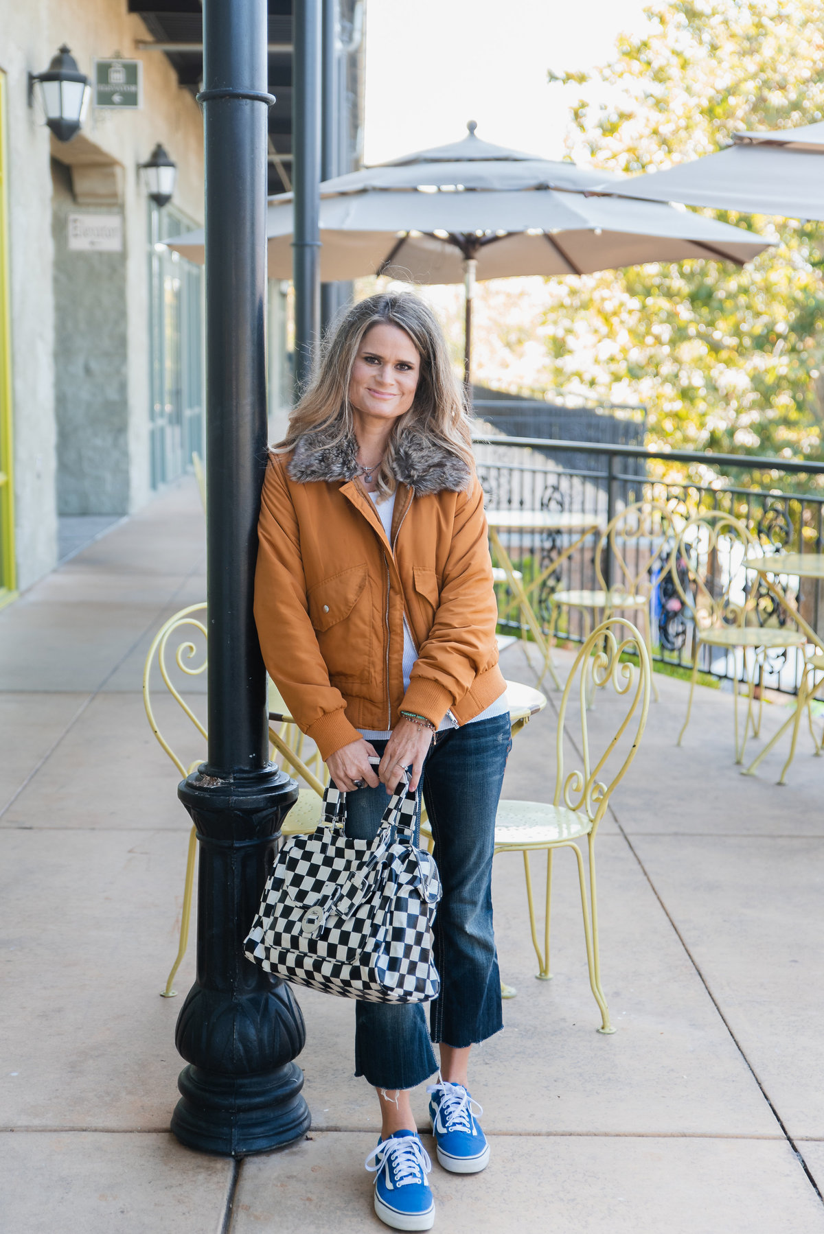 woman leaning against pole on cafe patio holding checkered bag