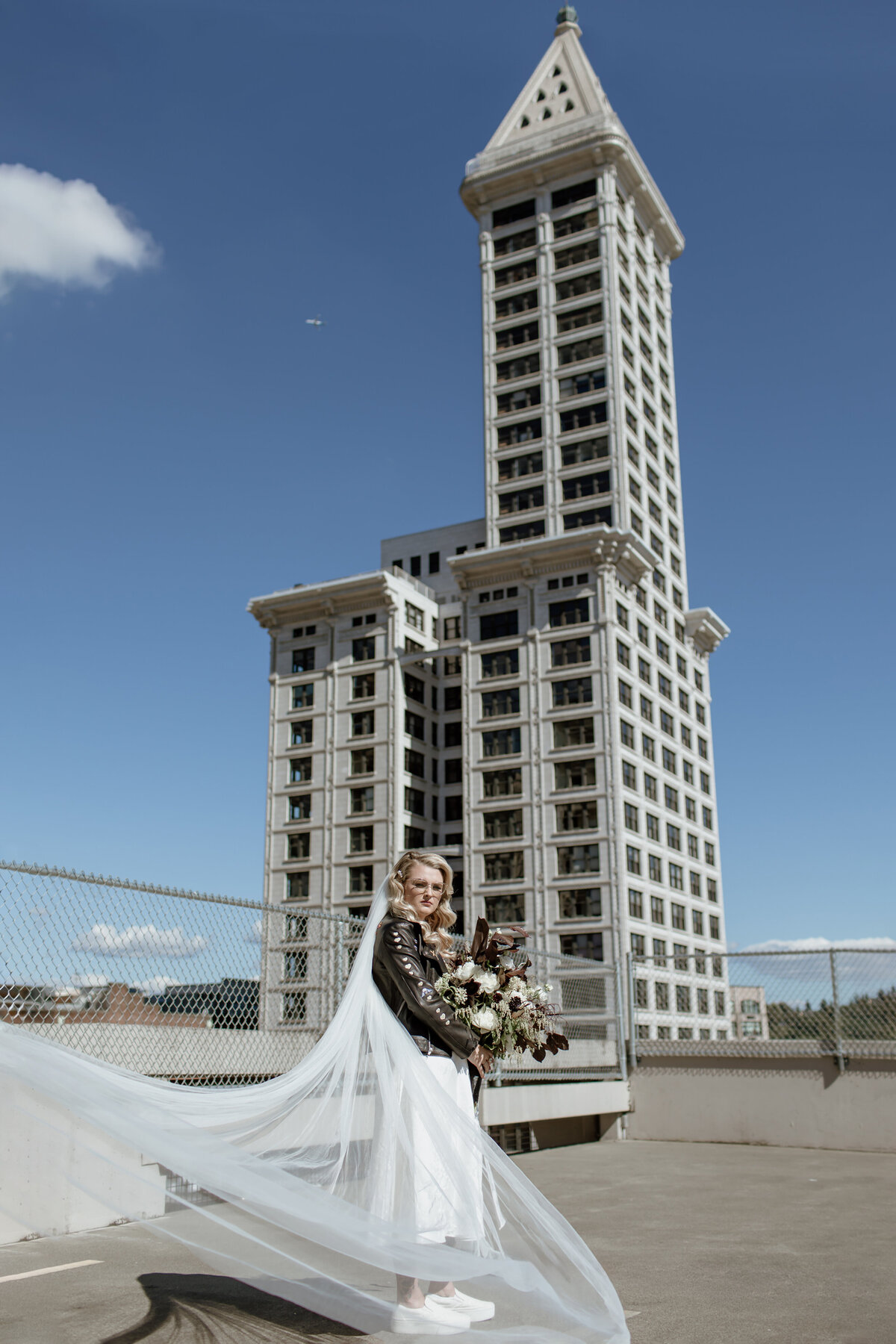 Bride in leather jacket on top of a Pioneer Square parking garage with the Smith Tower in the background. Captured by Fort Worth Wedding Photographer, Megan Christine Studio