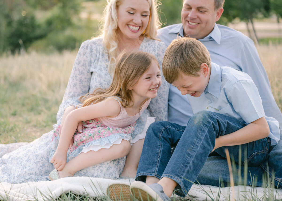 family laughing together in a beautiful summer field, photo taken by Highlands Ranch family photographer Maegan Ritterbush