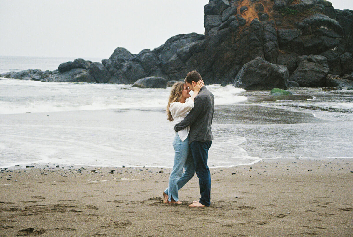 A couple embracing and kissing with the ocean behind them.