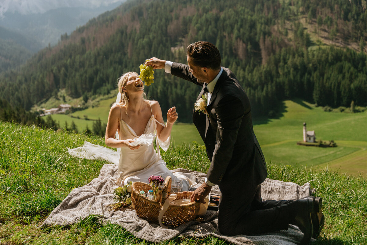 Bride and groom enjoying picnic on blanket in Val di Funes