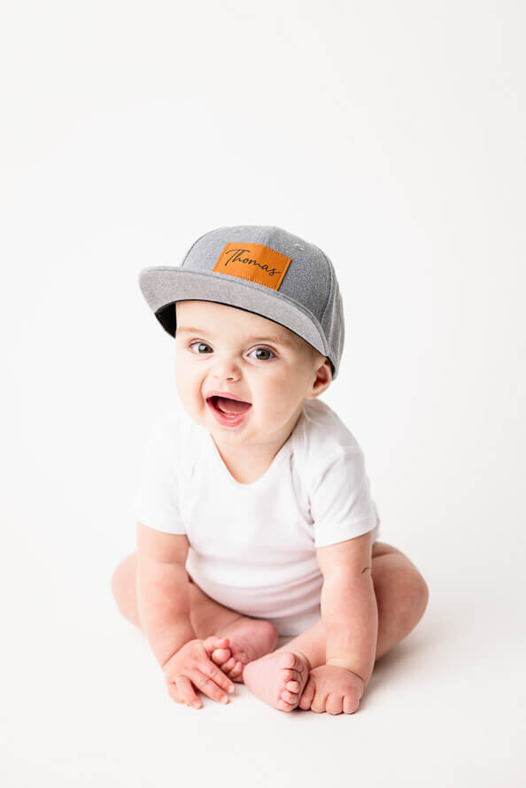 Baby boy in gray hat smiles for camera.