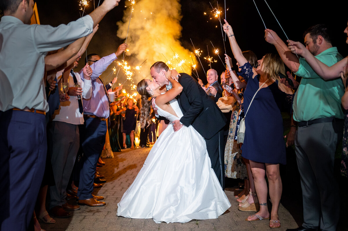 A groom dipping a bride in with smoke and sparklers behind them at the end of the night