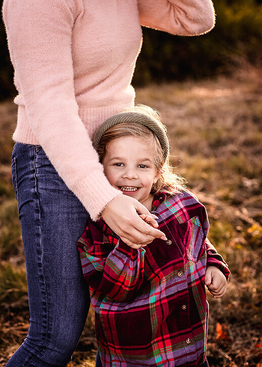 Little girl leaning on moms leg while holding hands in a field at Wagon Hill  in Durham NH