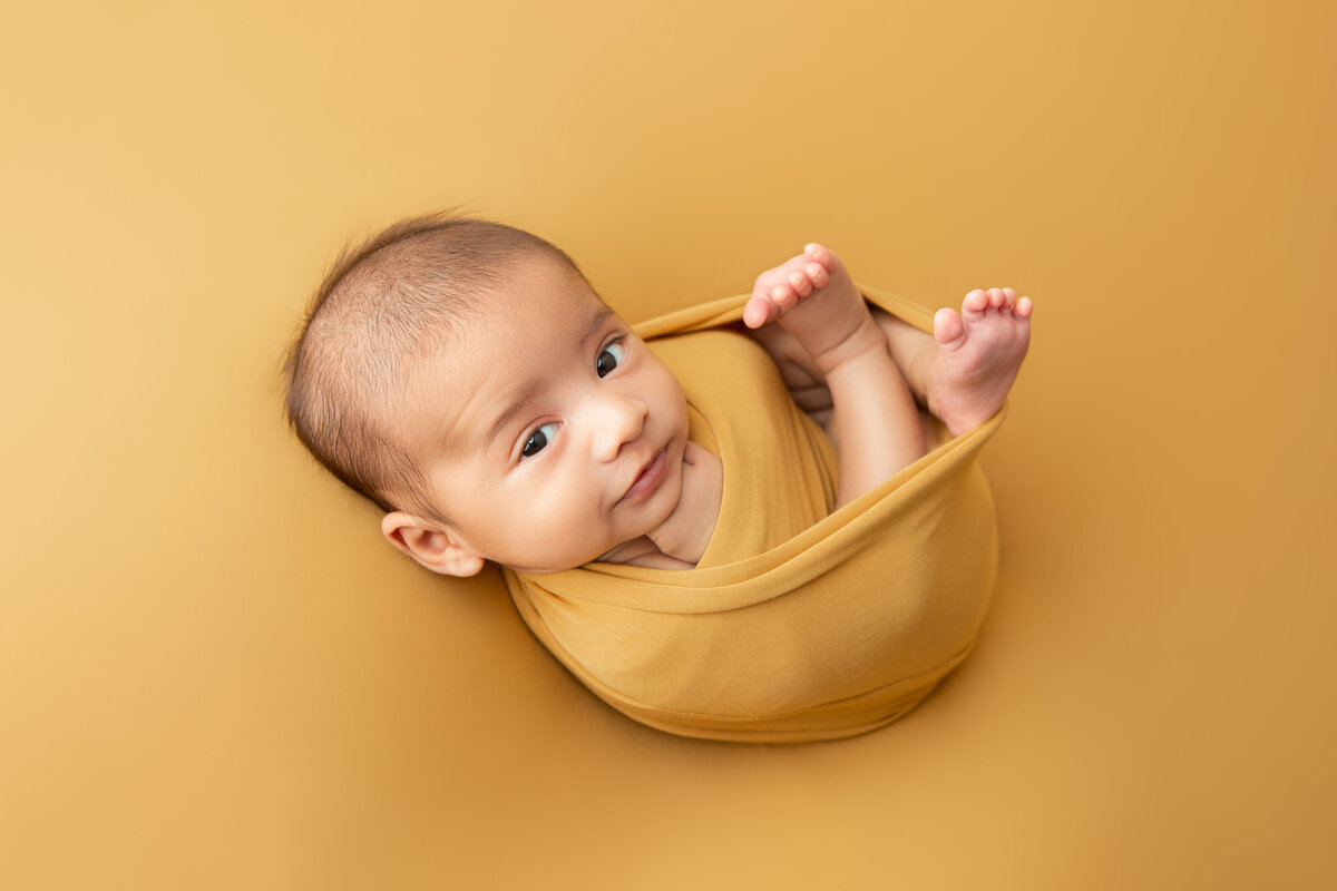 Studio wrapped newborn table posed on a mustard backdrop