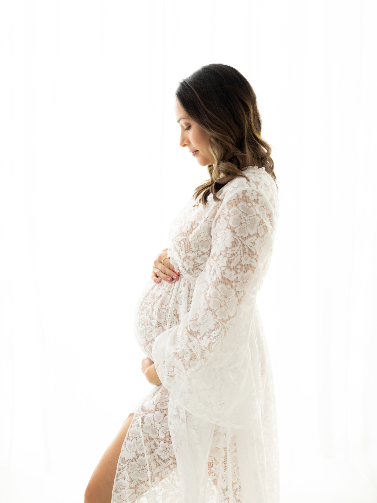 pregnant mother in white lace maternity gown holding baby bump for maternity photoshoot cleveland maternity photographer
