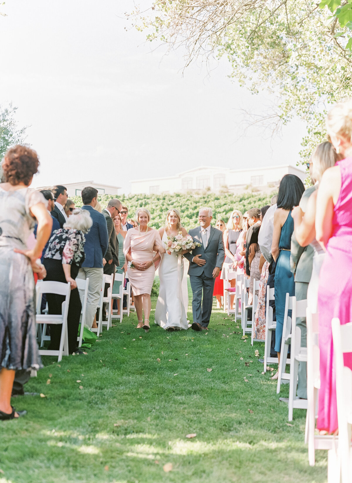 parents escort bride down the aisle with vineyards in the background