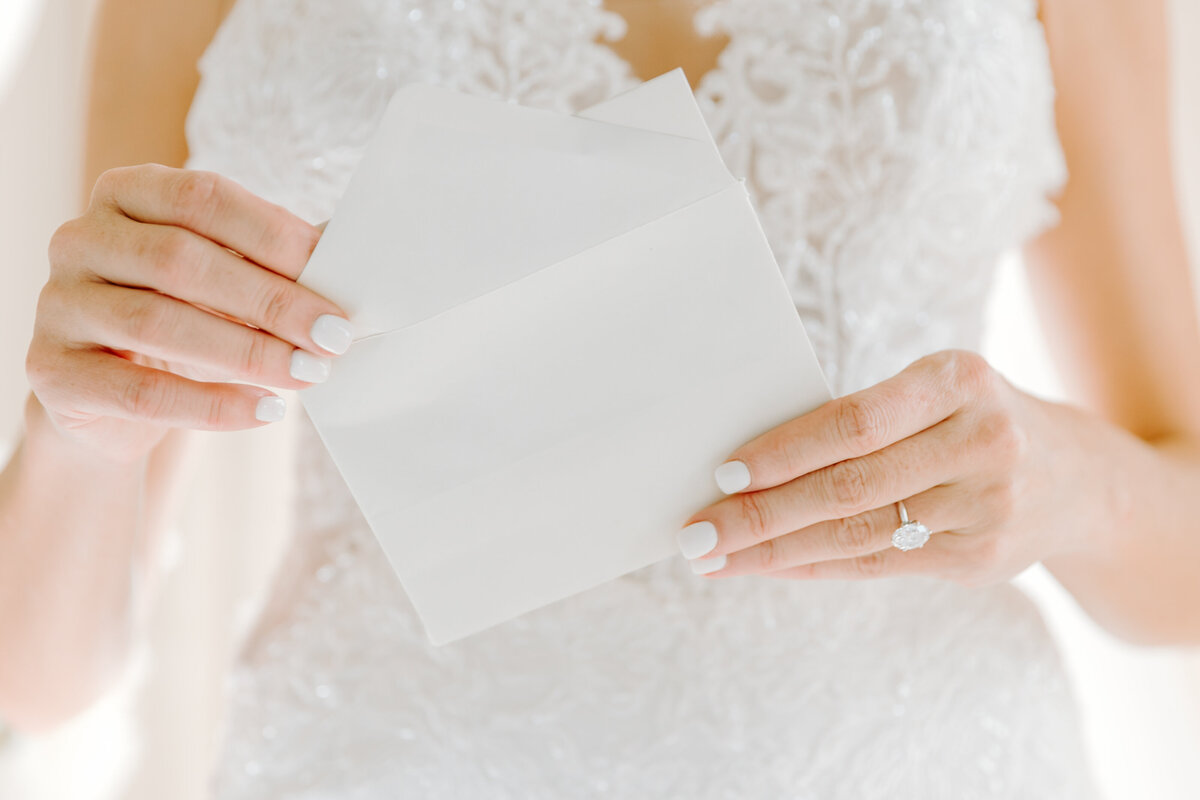 Bride opening letter from the groom in her elegant and sophisticated lace wedding gown before her wedding at The Dewberry. Captured by premier charleston wedding photographer, Sarah Beach Photography