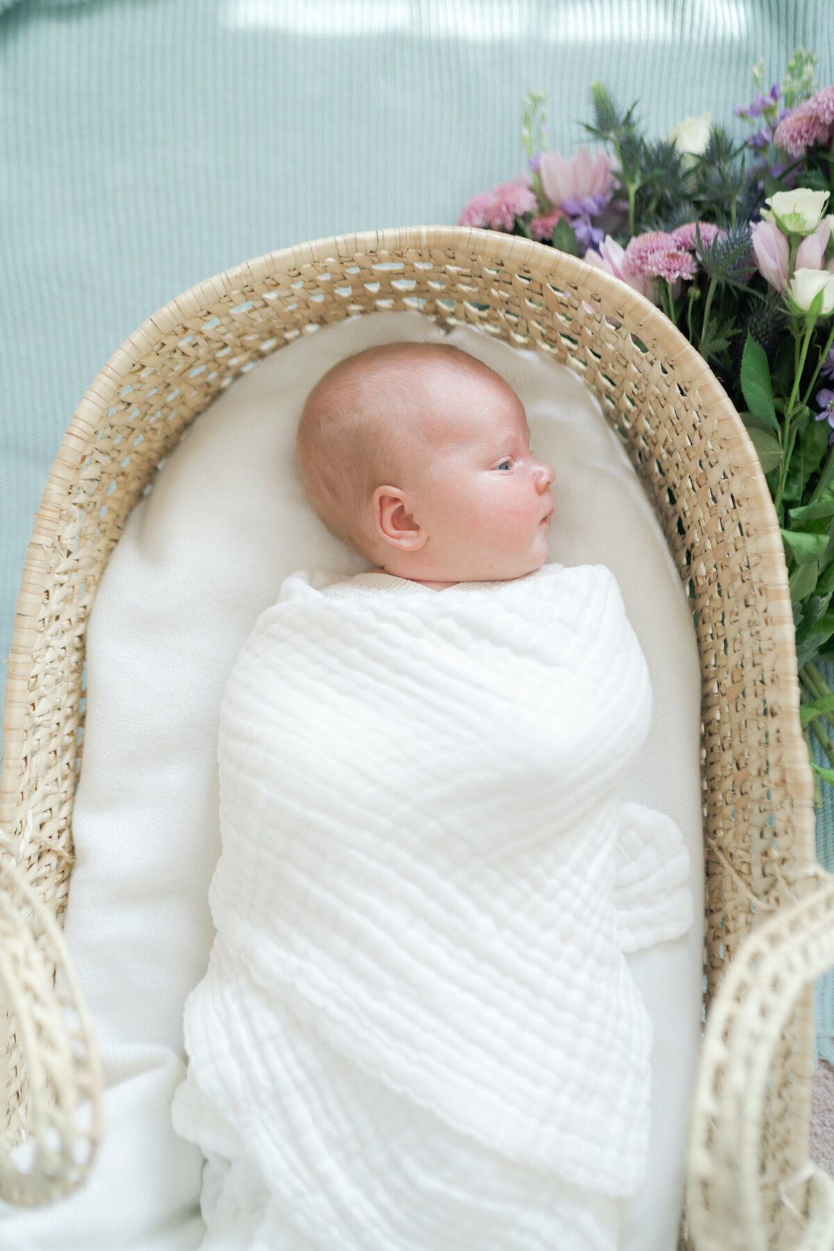 Newborn baby snuggly swaddled in a moses basket with flowers surrounding the outside by Oklahoma City Newborn Photographer courtney cronin