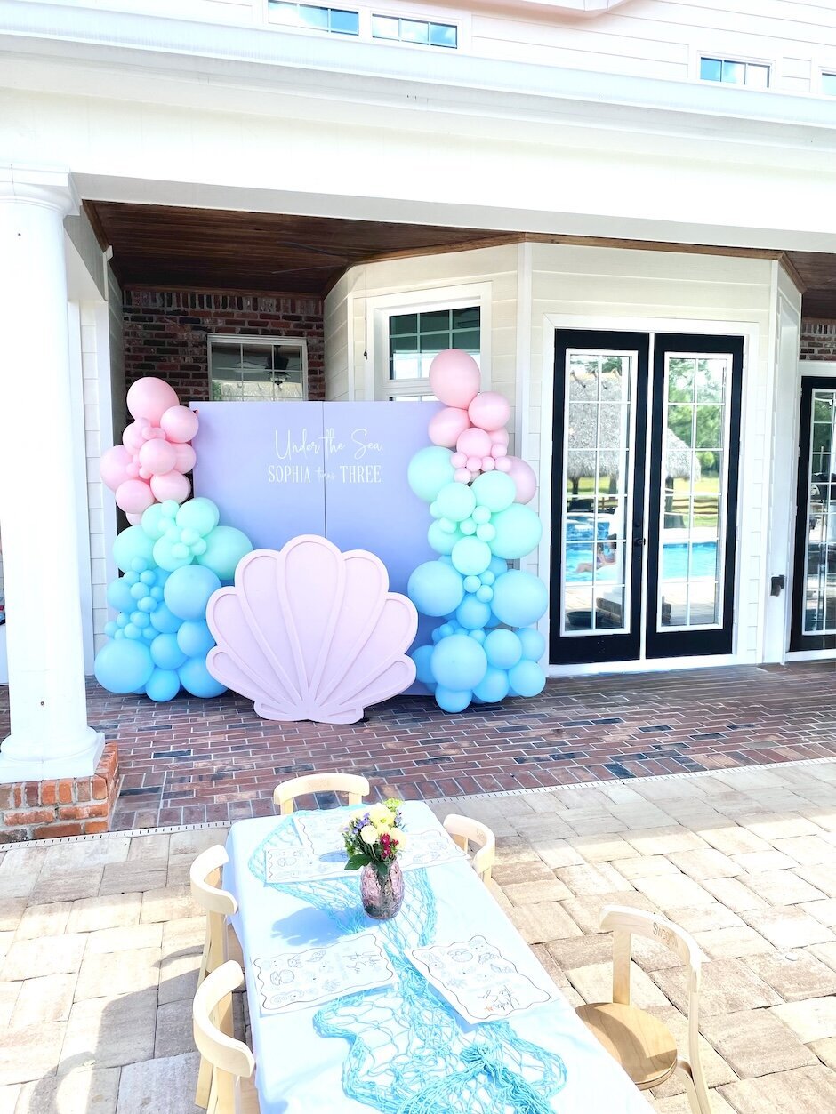 Balloons and backdrop in purple, blue, green and pink balloons with kid's table set up.
