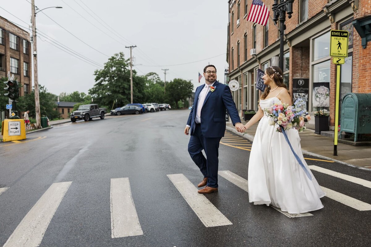 Bride and groom walk across Beacon's Main Street on their Roundhouse wedding day in the rain