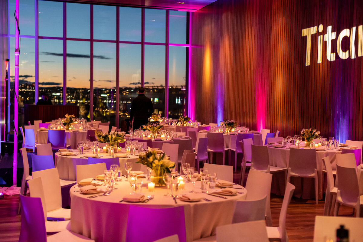 Elegant dinner tables illuminated with purple and amber lighting, Titan branding projected on the wall, overlooking the New York skyline.