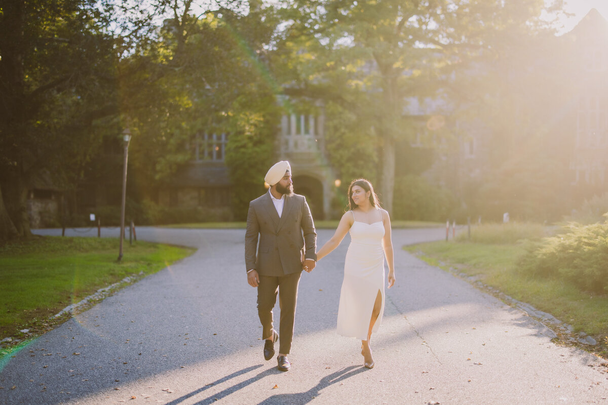 A sikh couple in cream clothing walking during golden hour in front of the skylands manor mansion at ringwood state park nj
