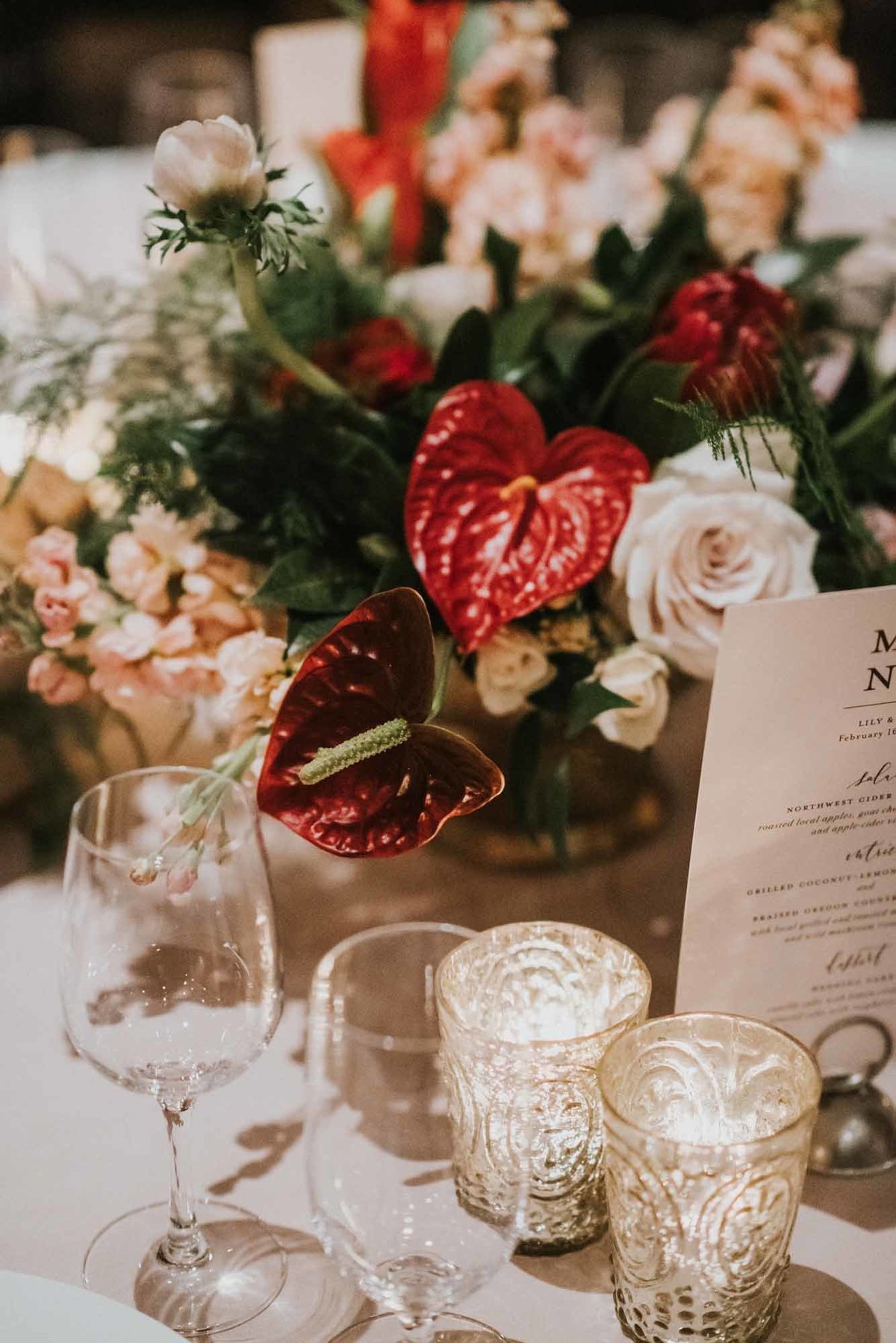 low centerpiece with red anthuriums, proteas, ivory roses, anemones, and greenery