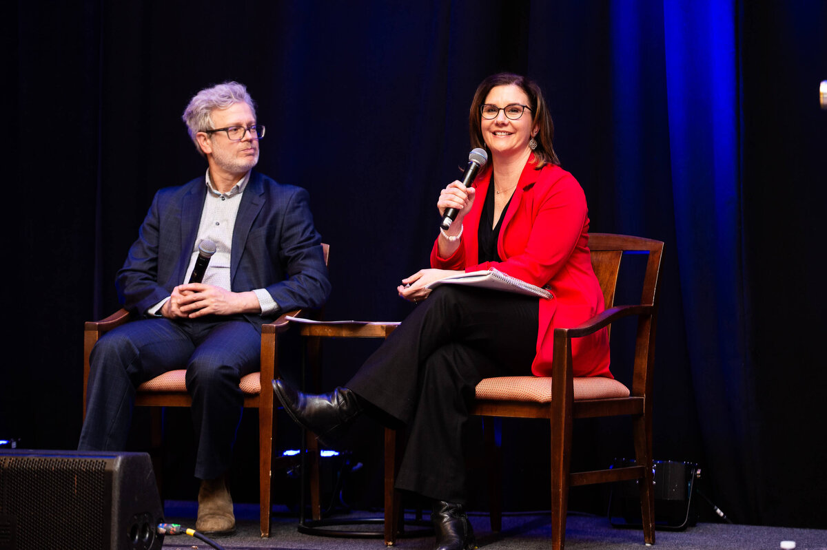 a woman in a red jacket talking into a microphone as part of a 2-day corporate conference at the Westin Hotel.  Captured by Ottawa Event Photographer JEMMAN Photography COMMERCIAL