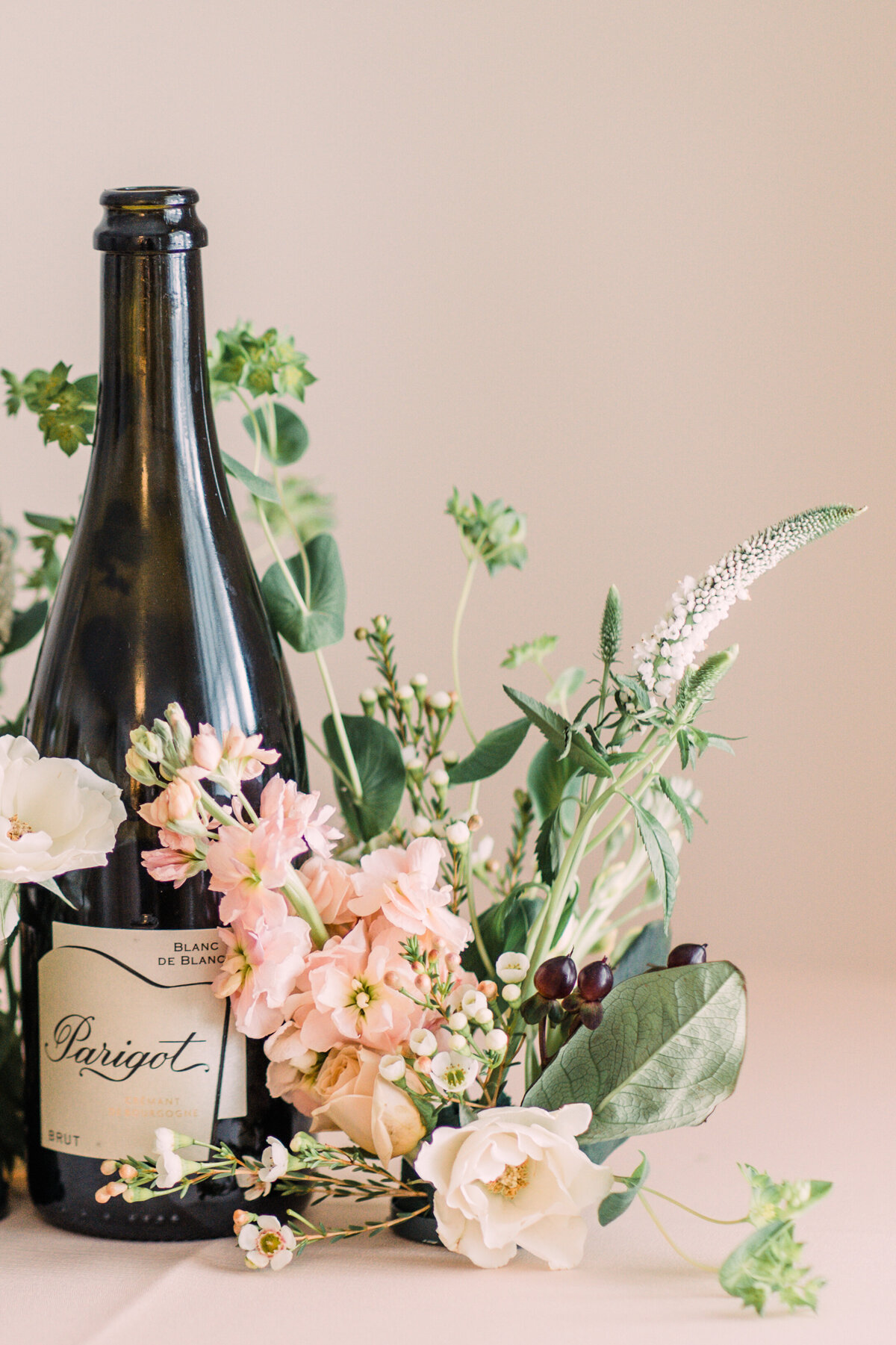 Closeup of a bottle of champagne with floral accents in pink, ivory, & burgundy at Cornman Farms