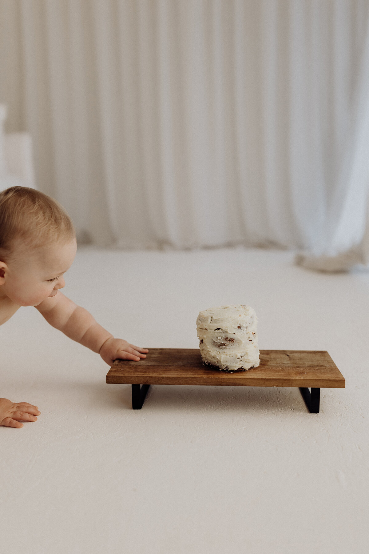 A little baby looking at her first birthday cake smash cake during her photoshoot with christchurch milestone photographer lucy jane