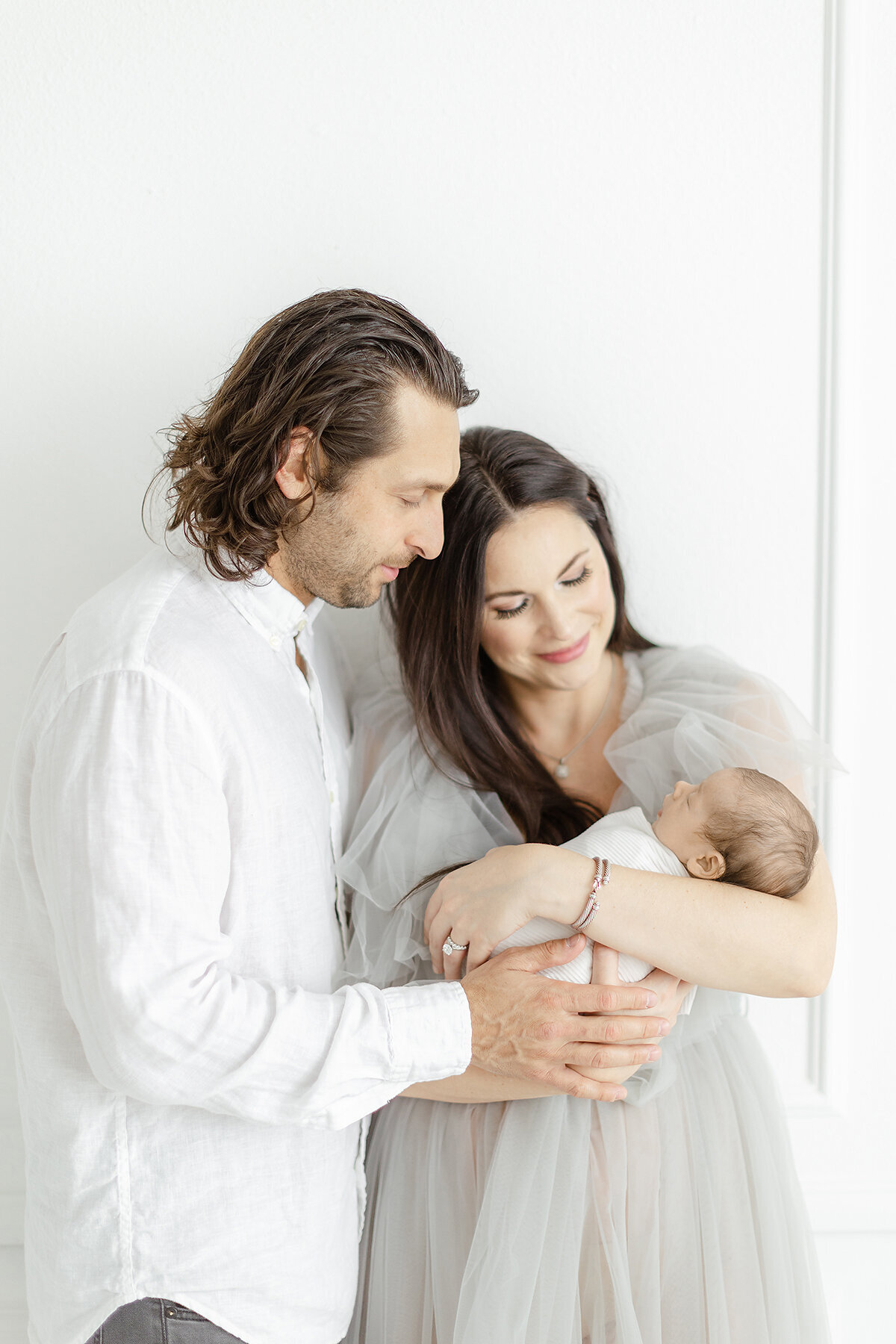 Close up photo of new parents to a newborn baby boy as they hold each other while they stand in a Dallas/Fort Worth photography studio posing for their babies newborn session.