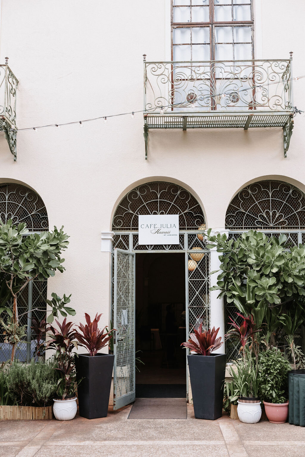 cafe julia metal doorway with balcony above and greenery surrounding