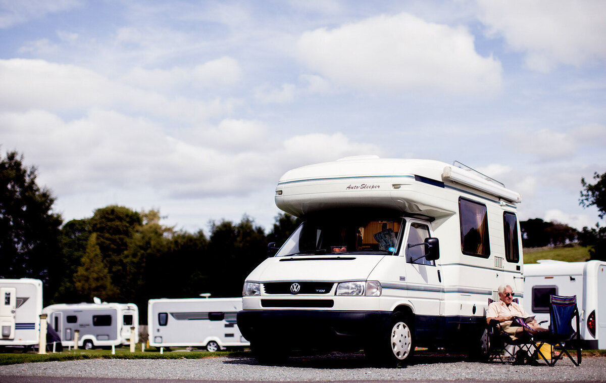  a man reading a magazine outside a motorhome with his feet up