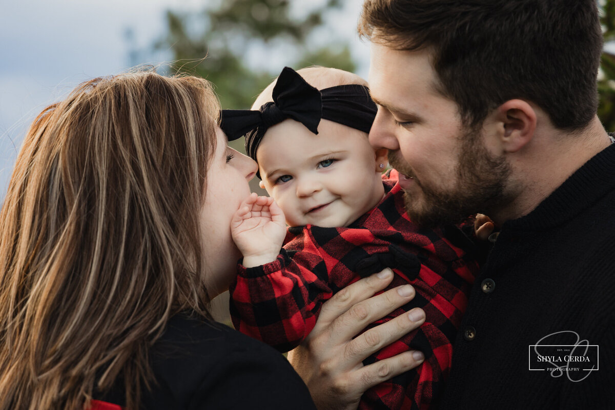 Baby looking at camera as mom and dad kiss her cheeks 