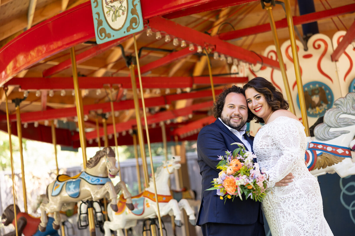 A bride and groom standing close together in front of a merry go round