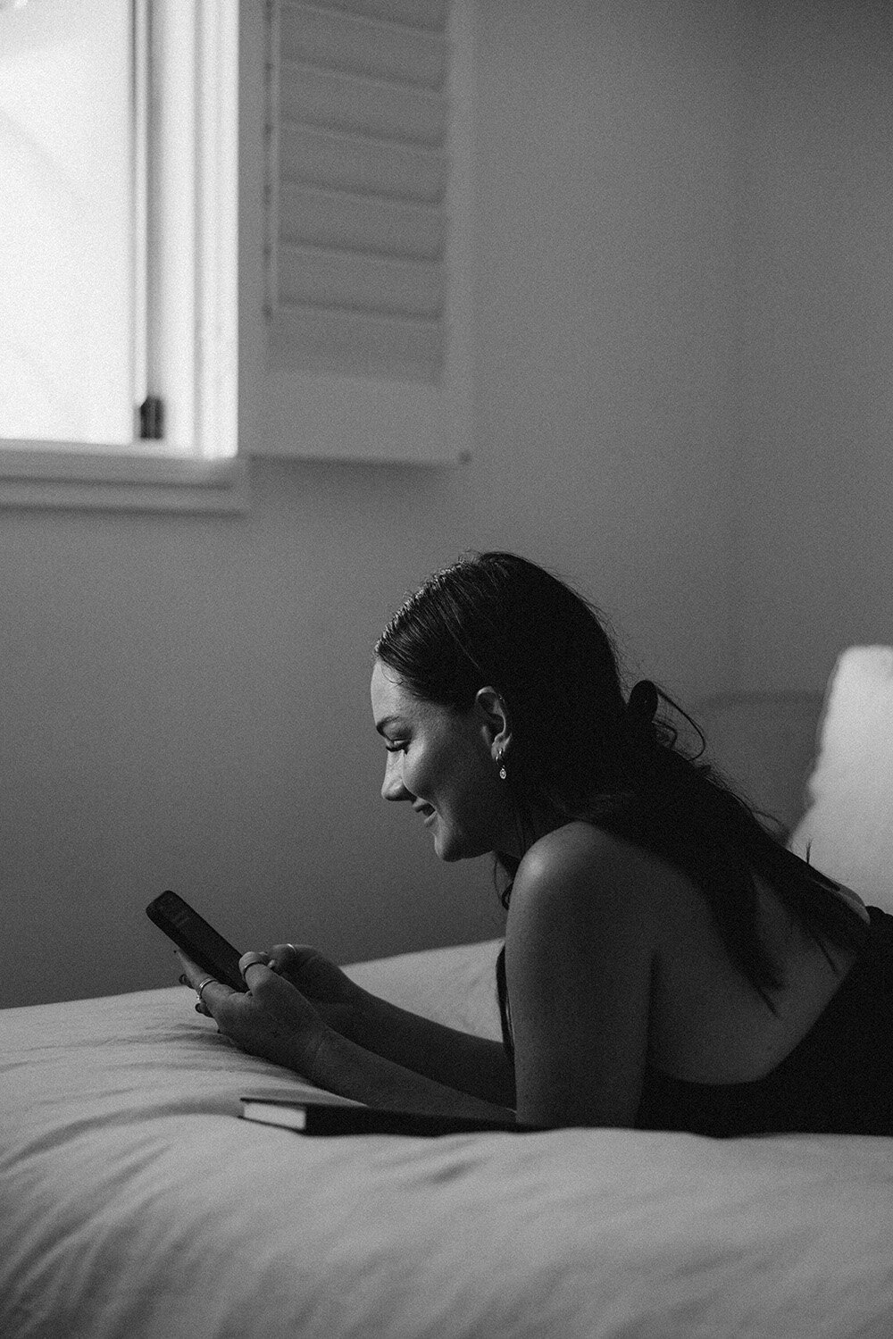 A sunshine-filled candid moment of a woman laughing while writing on her phone, captured in black and white by Sunshine Coast branding photographer.