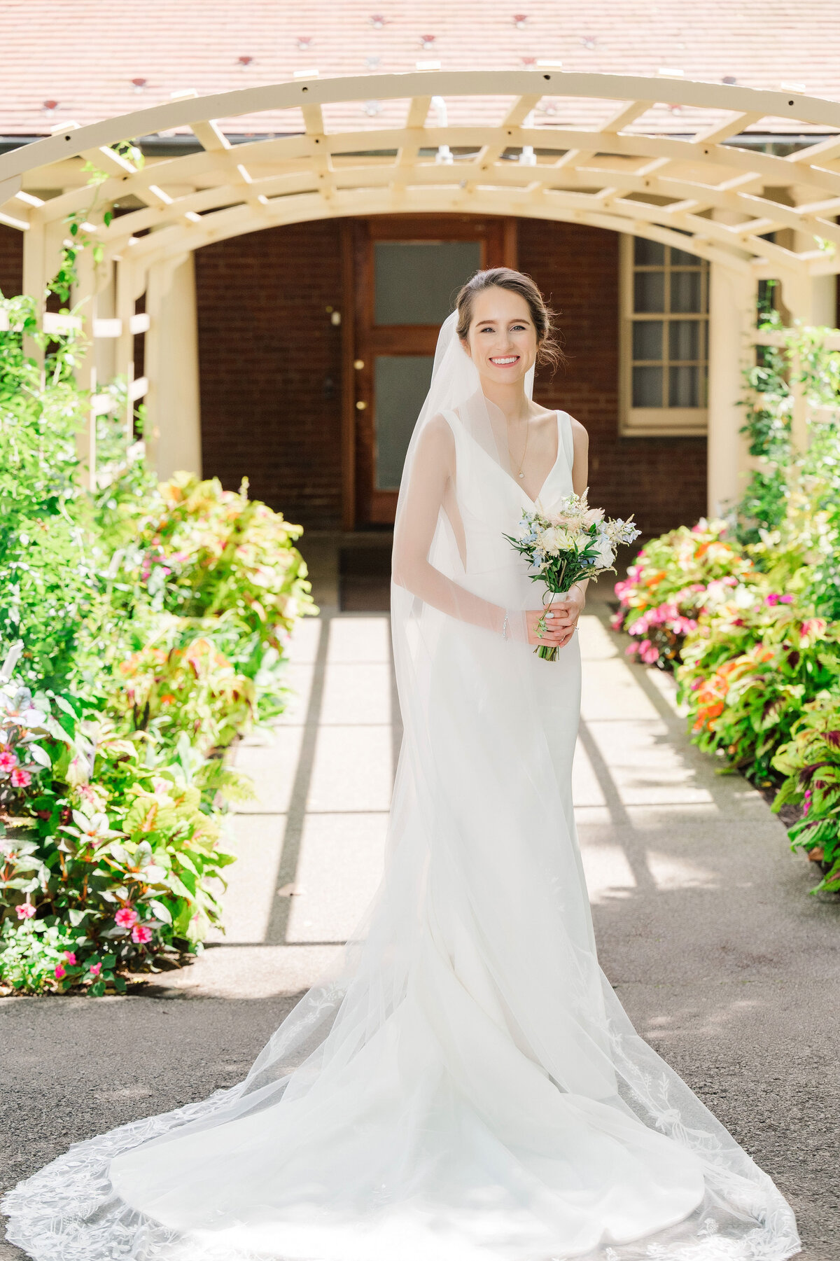 bride posing on wedding day in front of Frick Museum gardens and playhouse