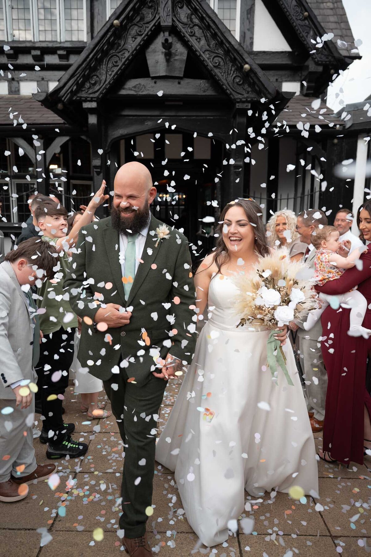 Confetti throw outside Worsley Court – bride and groom smiling surrounded by guests.