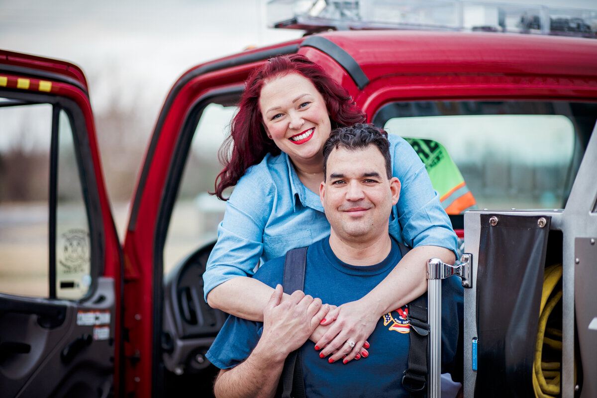 A man and women stand on a firetruck while embracing. Captured by Arkansas wedding photographer Photography by Karla.